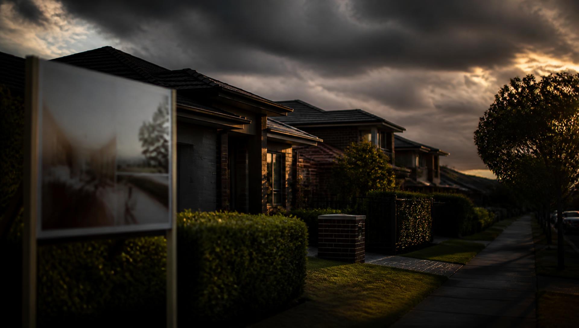Australian suburban street at dusk under heavy cloud with a for sale sign in the foreground