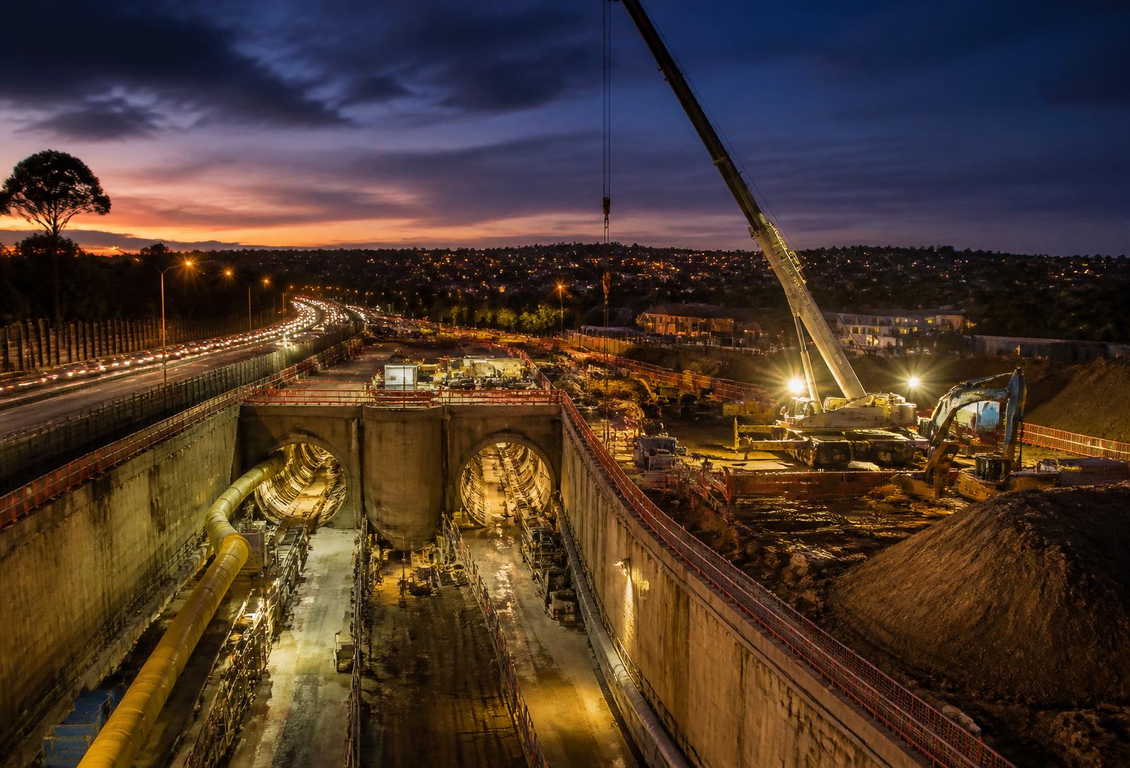 Major motorway tunnel construction site beside a suburban corridor at dusk